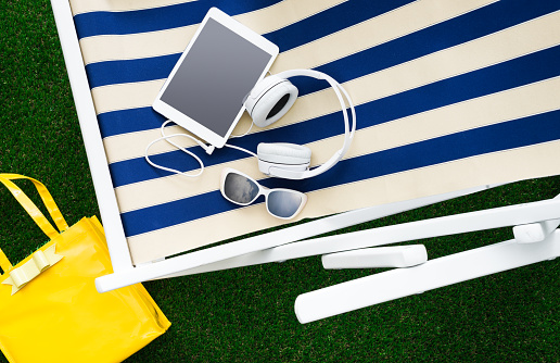 Striped deckchair in the garden with tablet and sunglasses: summertime, relax and sunbathing