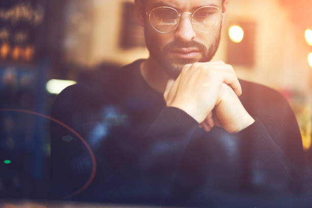 istock Close up of pondering trader in stylish eyeglasses thinking on solving problem.Cropped image of hipster guy in optical spectacles dressed in casual outfit analyzing information sitting indoors 907963374