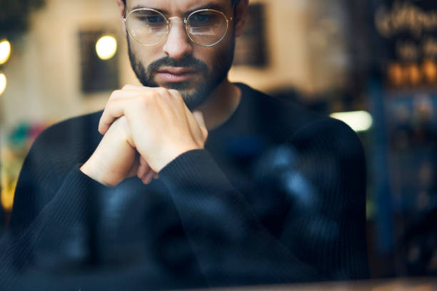 istock Close up of pondering trader in stylish eyeglasses thinking on solving problem.Cropped image of hipster guy in optical spectacles dressed in casual outfit analyzing information sitting indoors 907963424