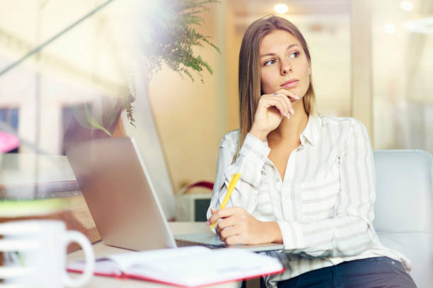 istock Thoughtful female student sitting at modern macbook computer and thinking on writing coursework in coworking space.Pensive young woman preparing for training seminar with laptop in office interior 907963774