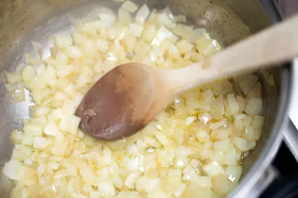 Onions frying in the pot with wooden spoon. Copy space available.