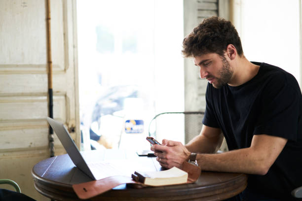 istock Young bearded man chatting on modern cellular via free 4G internet connection sitting at laptop computer and enjoying free time in cafeteria.Smart student checking email anf messaging on smartphone 907972900