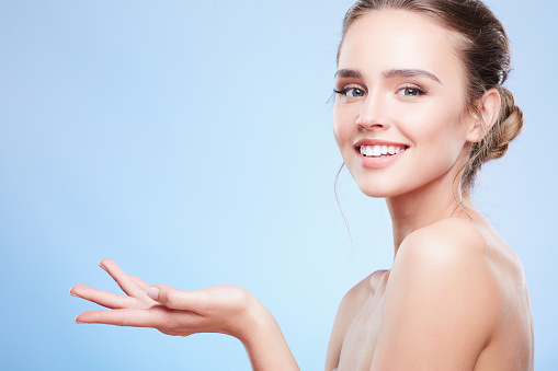 Beauty portrait of woman with stretched hand, semi profile. Head and shoulders of woman with nude make-up looking at camera and smiling, beauty concept, turned aside