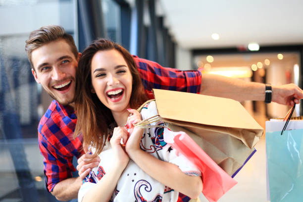 vendita, consumismo e concetto di persone - felice giovane coppia con borse della spesa che camminano nel centro commerciale. - shopping mall retail shopping sale foto e immagini stock