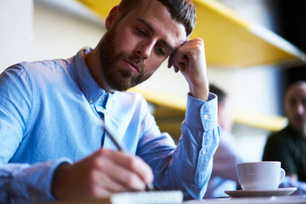 istock Thoughtful pensive male writer thinking about ideas for writing interesting story during free time.Contemplative businessman writing checklist in notebook sitting with coffee in cafeteria indoors 907985804