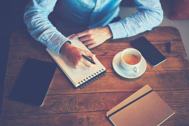 istock Cropped image of man's hand working at wooden table while writing checklist in notepad. Business man planning organizer schedule 907985836