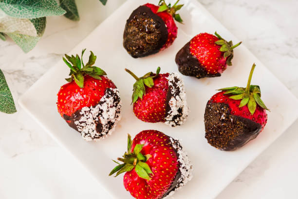 Fresh strawberries dipped in dark chocolate and coconut flakes with a cup of coffee in a white bowl. Breakfast for Valentine's Day. stock photo