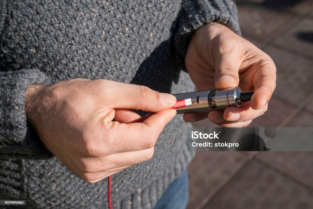A man charging an electronic cigarette in the park Electronic Cigarette Stock Photo
