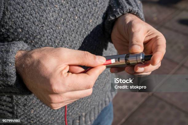 A Man Charging An Electronic Cigarette In The Park Stock Photo - Download Image Now - Electronic Cigarette, Pen, Ballpoint Pen