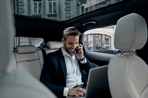Discussing business details. Handsome young man in full suit talking on smart phone and smiling while sitting in the car business journey stock pictures, royalty-free photos & images