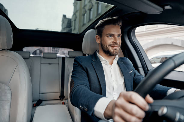 Success in motion. Handsome young man in full suit smiling while driving a car car interior photos stock pictures, royalty-free photos & images