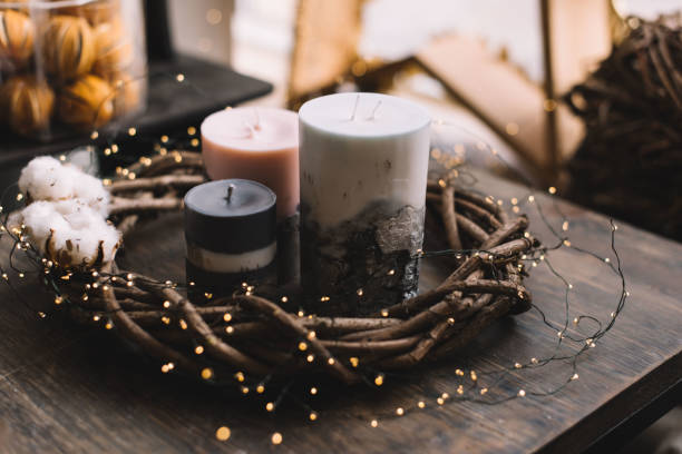 Beautiful festive hand-made candles (with concrete in it) and a wooden florist wreath around it with firefly garland on a rustic old wooden table with festive decoration on the background stock photo