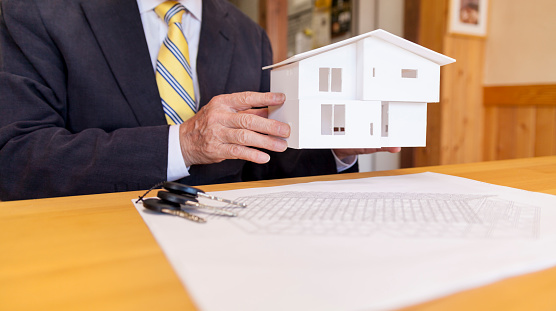 A Japanese senior businessman is showing a small model house.