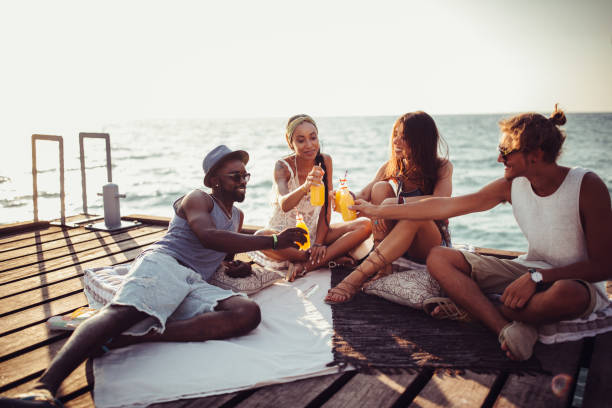 Multi-ethnic hipster couples on summer island holidays relaxing and toasting with orange juice on pier