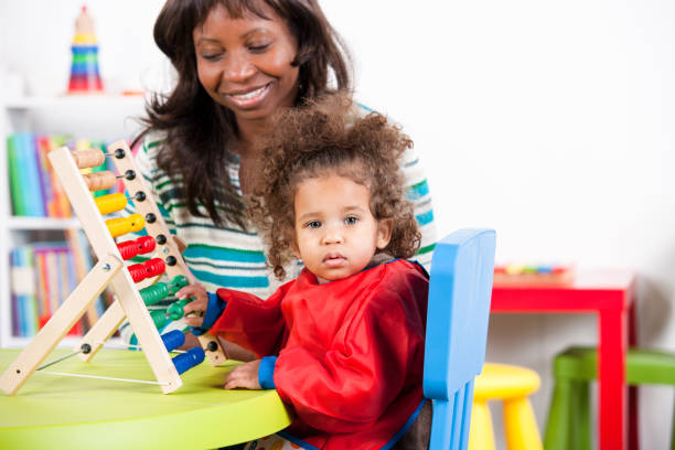 istock Smiling teacher by toddler playing with abacus 908002578