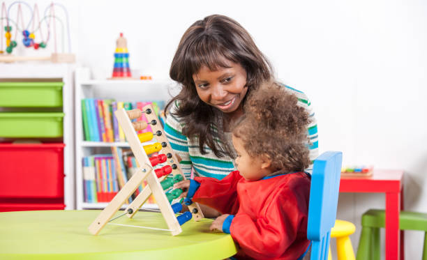 istock Teacher looking at baby playing with abacus 908002602