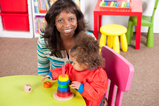 istock Teacher sitting by toddler stacking colorful rings 908002764