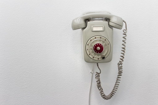 Old fashioned gray rotary telephone hanging on white wall.