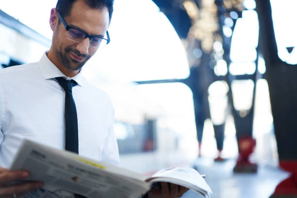 istock Pensive male entrepreneur reading newspaper publications while waiting for public transport on railway station, employee analyzing financial article standing on blurred background of platform 908008606