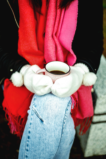Woman hands in white gloves holding a cozy mug with hot cocoa or coffee