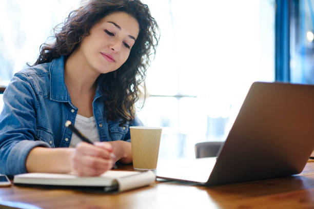 istock Pondering charming brunette student dressed in casual clothes writing down information while preparing for upcoming examination.Young cute hipster girl planning schedule during coffee break indoors 908009268