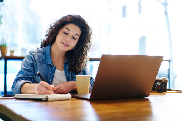 istock Thoughtful attractive female freelancer with curly hair notating information in notepad while working in loft coffee shop.Pensive student writing down notes during preparing for coursework 908009284