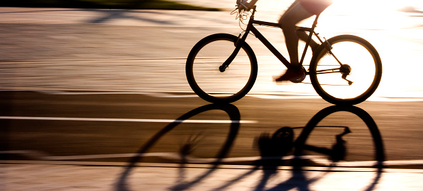 Blurry panning silhouette and shadow of a cyclist on a biking lane in summer sunset back light high contrast