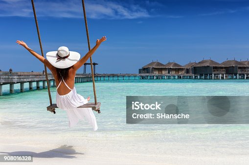 istock Happy female traveller on a swing at a tropical beach 908016328
