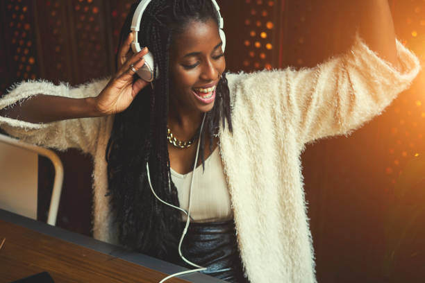 giovane allegra femmina hipster in abbigliamento casual che ascolta musica tramite grandi cuffie moderne bianche, afro american teen girl ricreare mentre si godono le canzoni preferite dalla playlist seduta al bar al chiuso - recreate foto e immagini stock