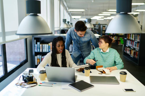 istock Crew of male and female international students analyzing information from websites while brainstorming in university library creating media marketing project using modern technologies and wifi 908020290