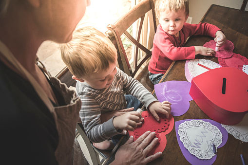 A stock photo of a mother making Valentines day crafts with her identical twin sons.