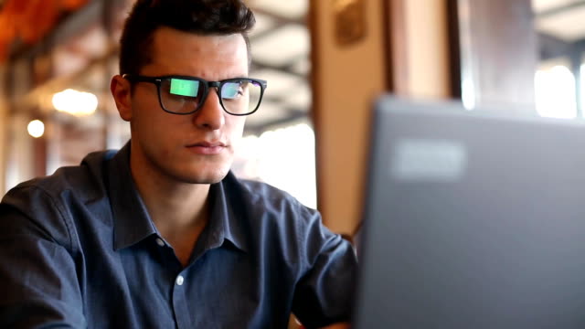Reflections of laptop monitor screen in man's glasses. Portrait of young caucasian freelancer businessman working and browsing internet in office. Hacker at work stealing accounts database