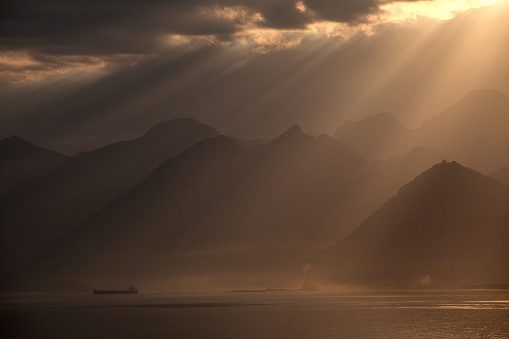 Sunbeams and dramatic cloudscape in Mediterranean city of Antalya, Turkey. The dominant color is orange due to sunset time of day. No recognizable people are seen in frame. Bey Mountains are seen. Shot with a full frame DSLR camera.