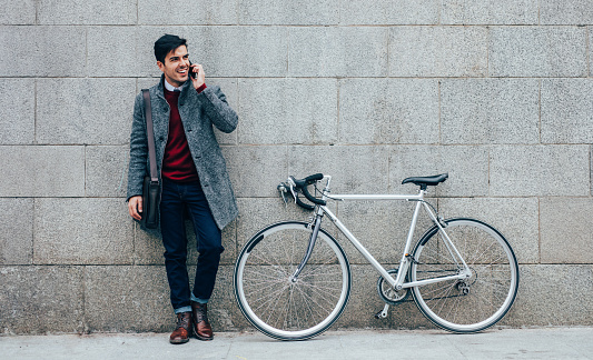 Elegant man with a bicycle using a smart phone in the city.