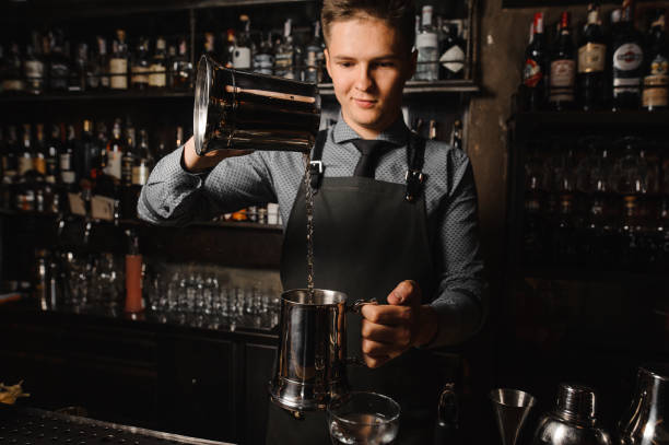 istock Young barman pouring a clear alcoholic drink on the bar counter 908041574
