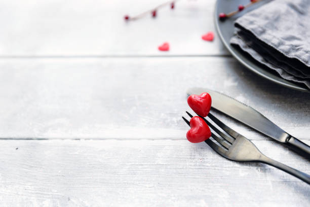 istock Festive table setting for Valentine's Day with fork, knife and hearts on a white wooden table. Space for text. Top view. 908045056
