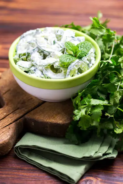 Traditional Indian cuisine. Homemade cucumber raita with yoghurt, garlic, mint, cilantro and spices on wooden background. Greek tzatziki sauce. Copyspace, top view.
