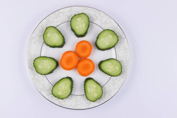 Sliced cucumbers and carrots on a plate, fresh vegetables, minimalism, empty space, top view, cucumbers and carrots on white background, healthy food, diet, packaging design