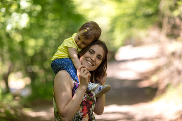 istock Mother carrying her daughter on shoulders in nature 908091672
