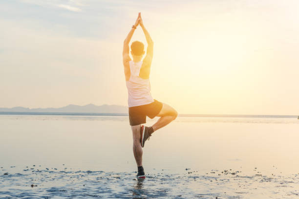 istock Young asian man doing yoga exercise at sunset beach 908126298
