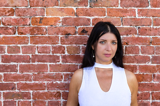 Stylish dark haired thoughtful woman posing in front of a red brick wall with copy space looking at camera