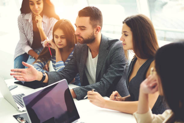 istock Diversity group of young students listening to coach explanation during lesson about using technology, colleagues sharing ideas about presentation of project planning watching video on laptop 908130864