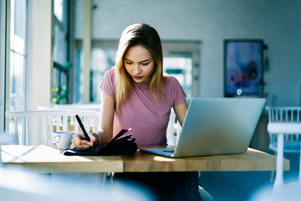 istock Concentrated female student working on project in cafe interior browsing information from internet, pensive skilled manager planning strategy for startup noting ideas and making checklist in notepad 908130992