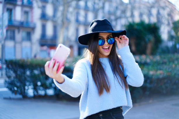 istock Joyful attractive woman emotionally posing for telephone camera while making selfie walking at urban setting.Positive cute hipster girl enjoying free time during strolling in the city 908131246