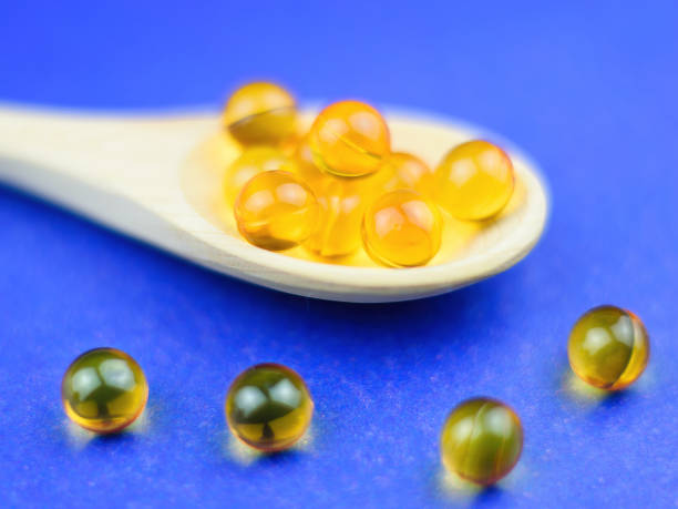istock Fish oil capsules in a wooden spoon on a blue background. Selective focus. 908155240