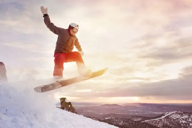 Snowboarder jumps against sunset sky and mountains