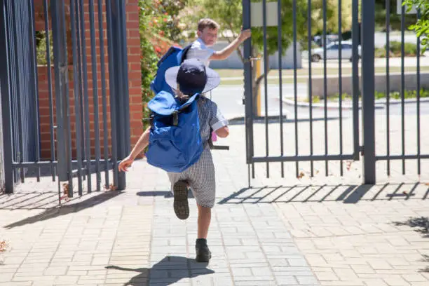 Two school children running out the school gate at the end of the day.