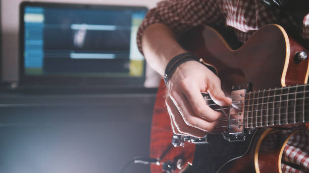 istock Young musician composes and records soundtrack playing the guitar using computer and keyboard 908186490
