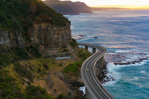 Aerial view of bridge along cliff edge and ocean Aerial view of bridge along cliff edge and ocean with traffic. Sea Cliff Bridge view on sunrise. Illawarra, New South Wales, Australia sea bridge stock pictures, royalty-free photos & images