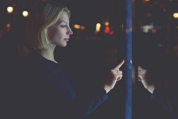 istock Caucasian female using automated teller machine with big digital screen while standing in night city out-of-focus lights, woman verifies account balance on banking application via modern device icon 908210296
